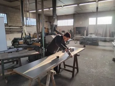 Artisan travaillant une longue planche sur tréteaux dans un atelier de menuiserie