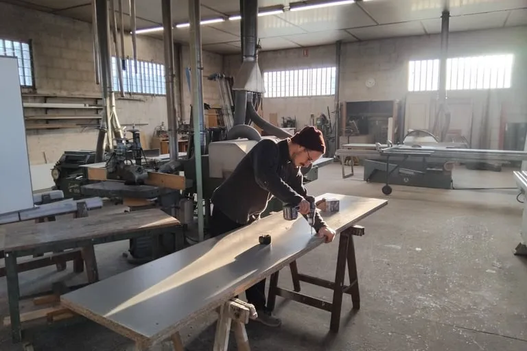 Artisan Atout Bois Condrieu appliquant une finition sur une planche dans l'atelier de menuiserie